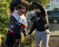 Two people wearing masks holding their arms towards each other making the shape of a heart