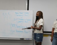 Two women pointing to a whiteboard