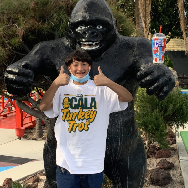 Child standing in front of a gorilla statue holding two thumbs up