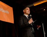 Person giving a speech in front of an orange banner