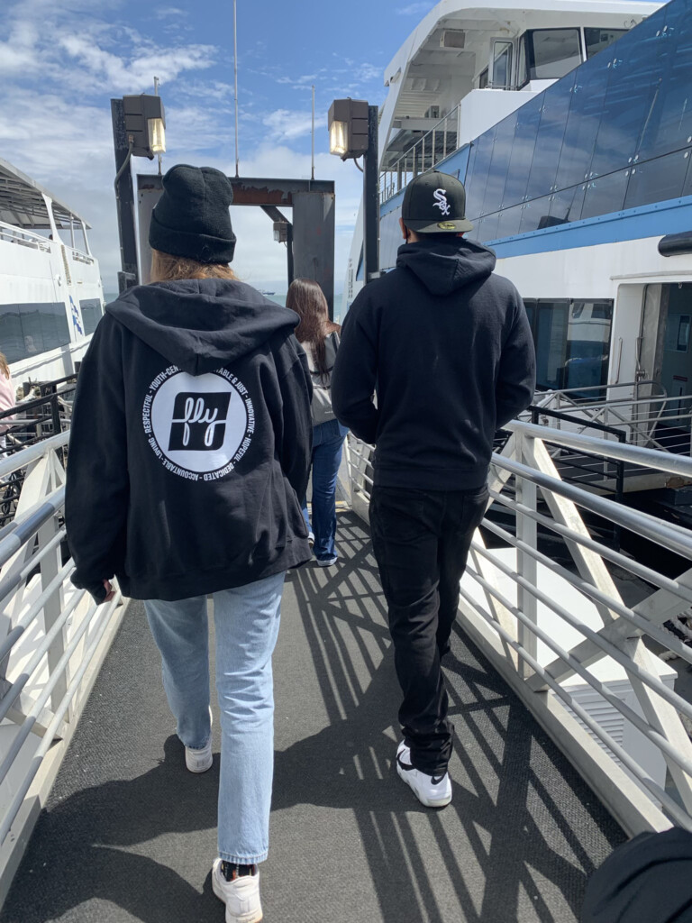 Two people walking away with the FLY logo on the back of their hoodie